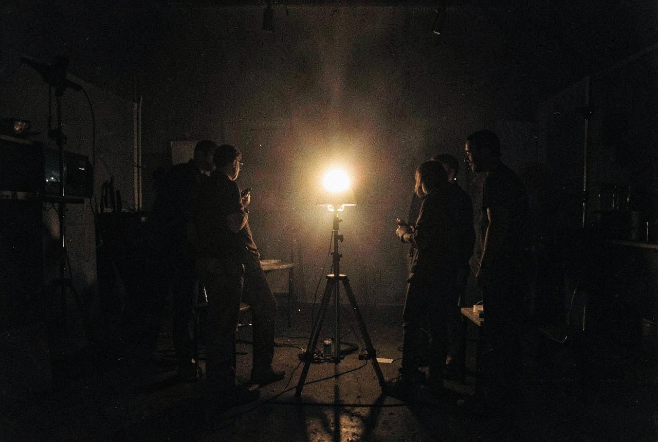 A small crew silhouetted around a single lamp on a dark set