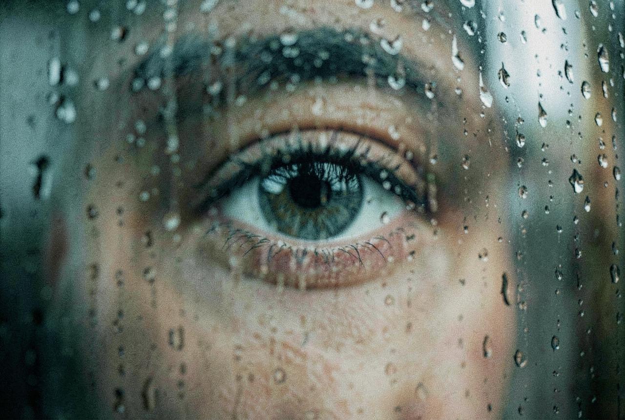 Close-up of an eye behind a rain-streaked window